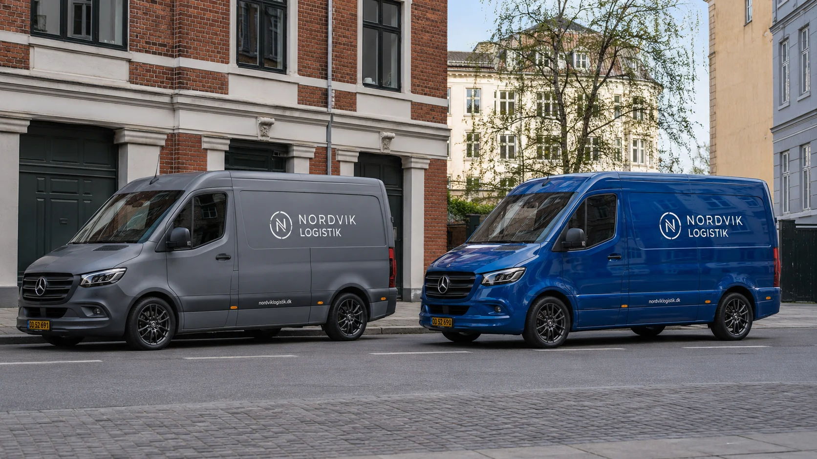 Matte grå varevogn ved siden af blank blå varevogn med firmalogo på en dansk gade