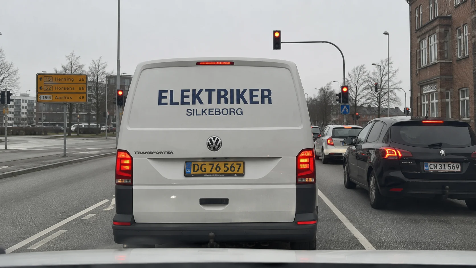 Hvid varevogn med tydelig elektriker-tekst på bagdørene holder for rødt i dansk bytrafik